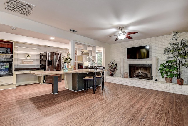 kitchen with visible vents, a brick fireplace, ceiling fan, wood finished floors, and black appliances