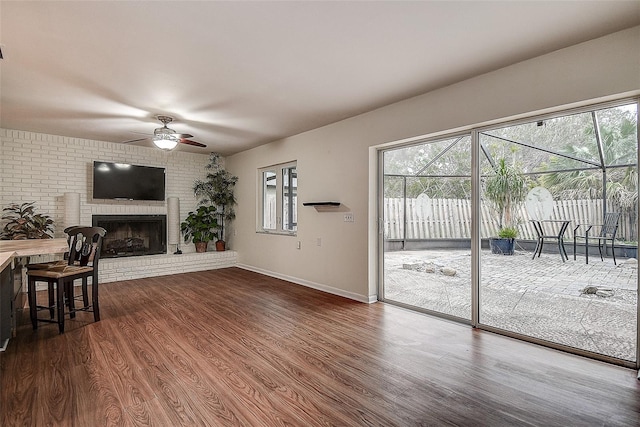 living room featuring a brick fireplace, baseboards, dark wood-style floors, and a ceiling fan