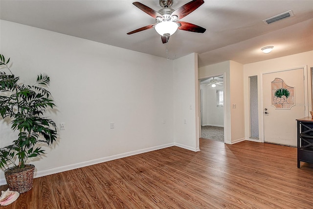 spare room with a ceiling fan, visible vents, baseboards, and wood finished floors