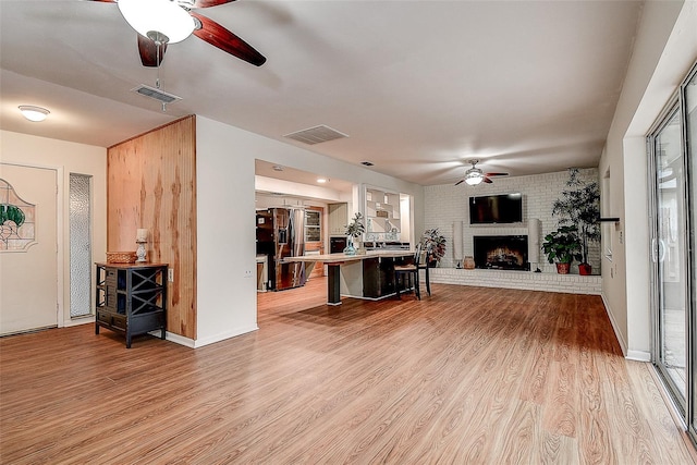 living area featuring light wood-type flooring, a fireplace, visible vents, and a ceiling fan