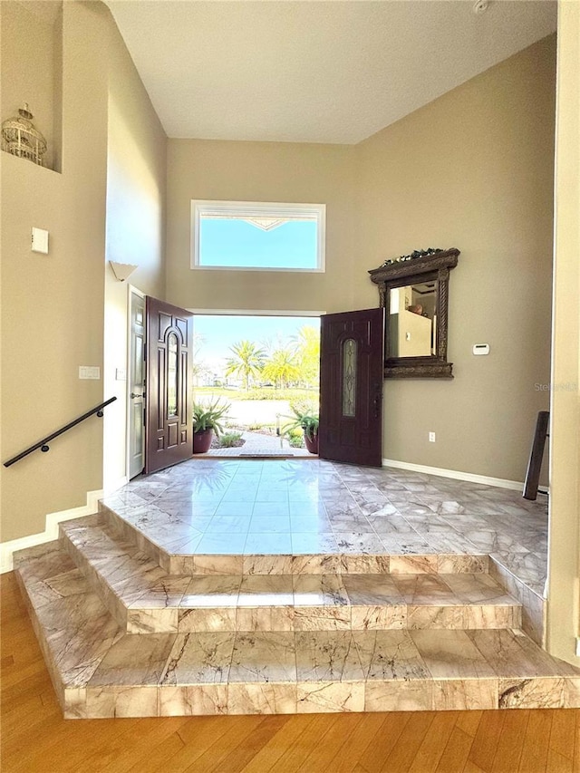 foyer entrance featuring a towering ceiling, baseboards, and wood finished floors