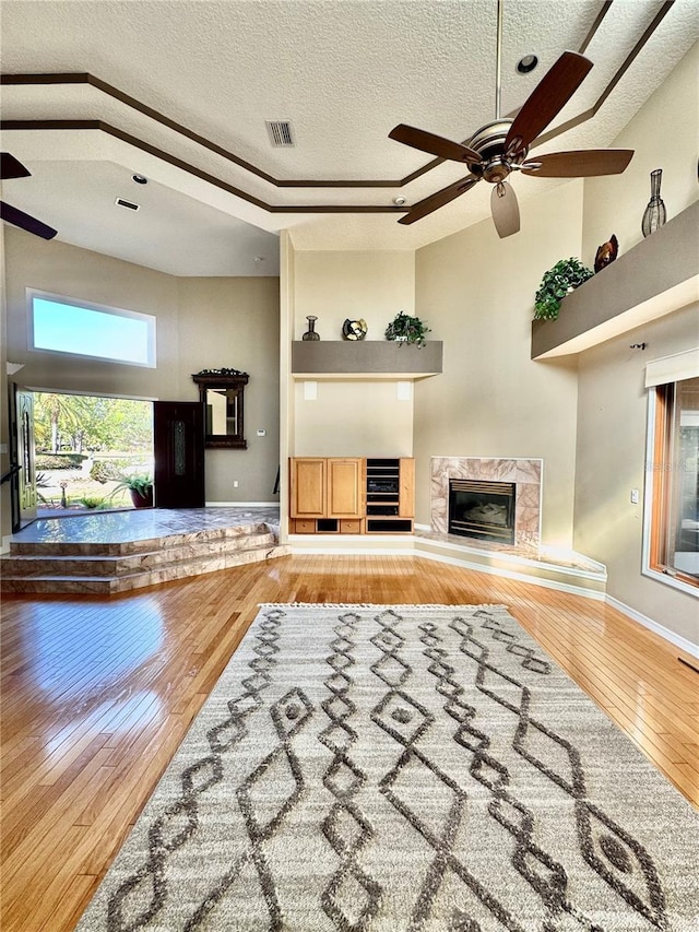 living area with a fireplace, visible vents, a towering ceiling, ceiling fan, and hardwood / wood-style flooring