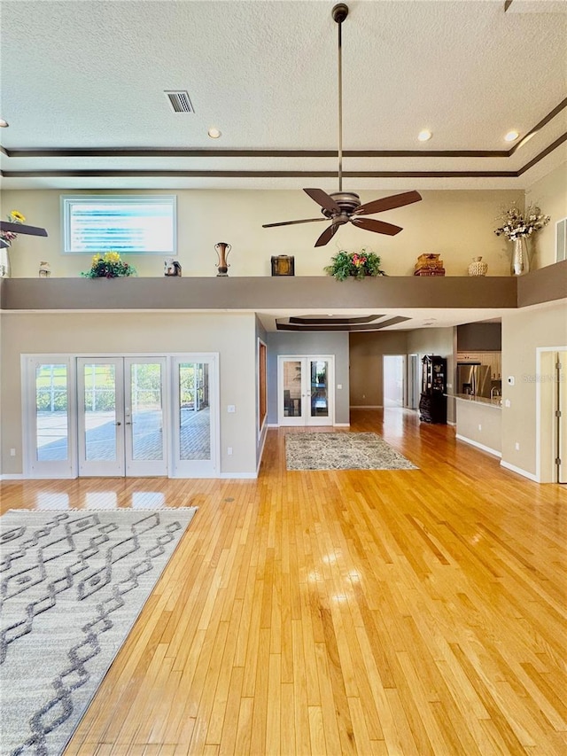 unfurnished living room featuring french doors, a high ceiling, wood-type flooring, and a textured ceiling