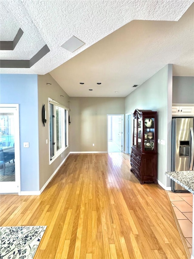 unfurnished living room with baseboards, plenty of natural light, light wood-style flooring, and a textured ceiling