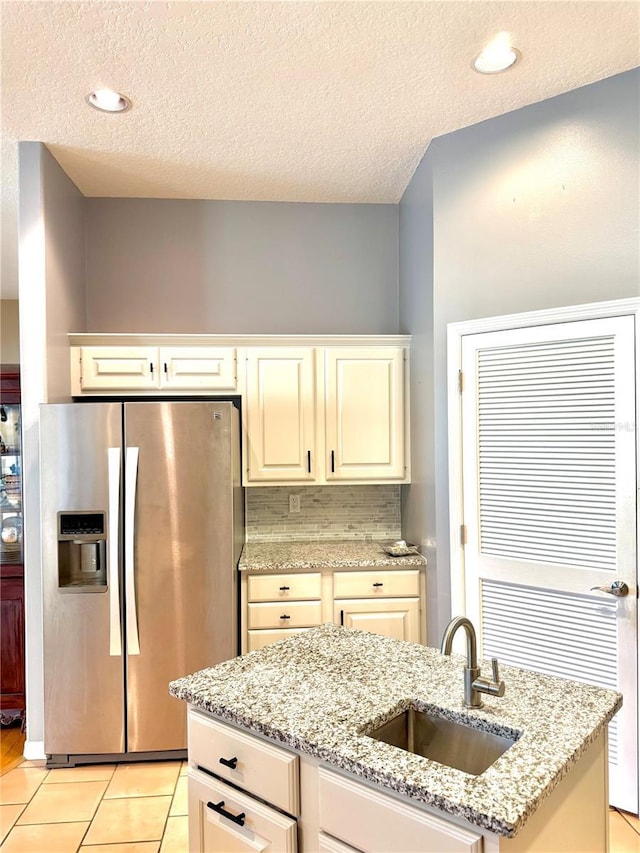 kitchen with tasteful backsplash, a textured ceiling, stainless steel refrigerator with ice dispenser, a sink, and light tile patterned flooring