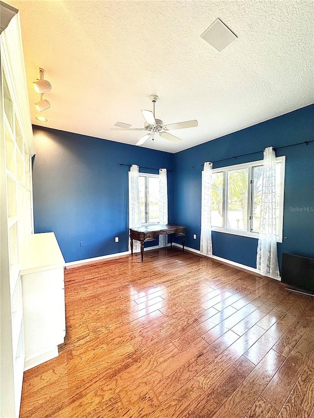 spare room with a wealth of natural light, a textured ceiling, a ceiling fan, and wood finished floors