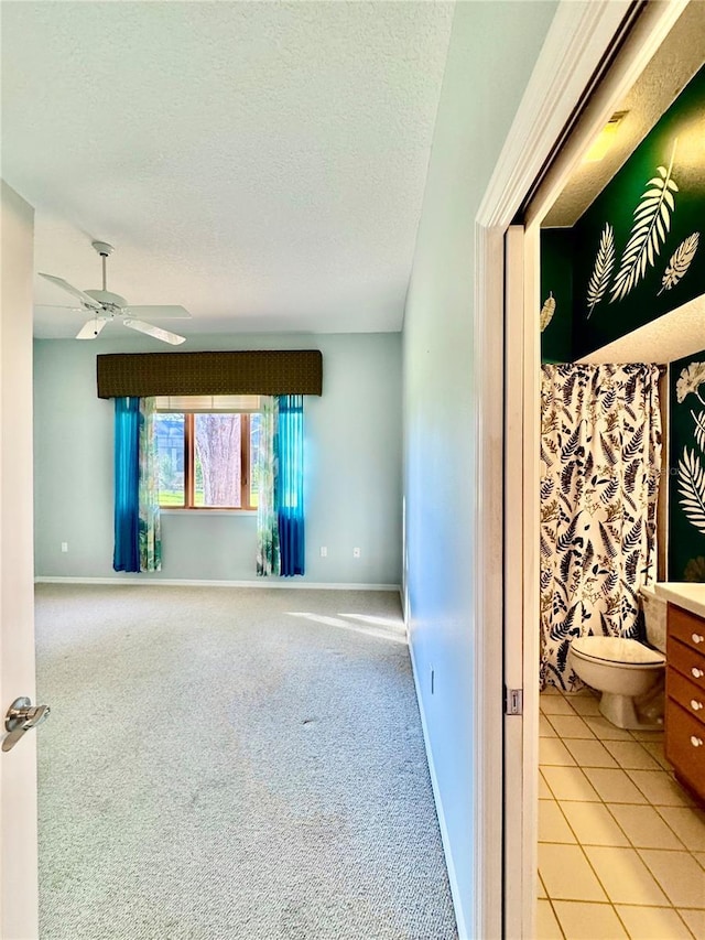 empty room featuring light carpet, ceiling fan, a textured ceiling, and baseboards