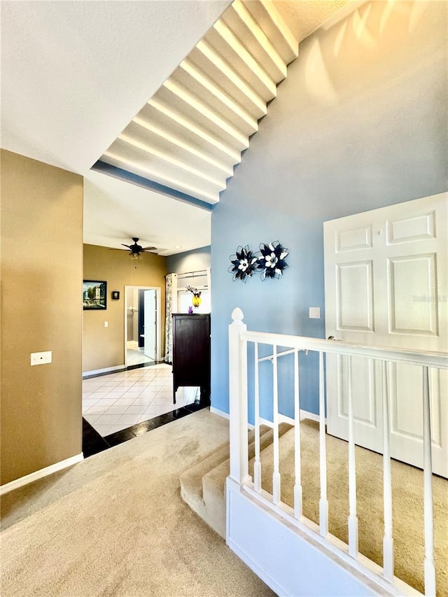 hall with carpet floors, an upstairs landing, baseboards, and tile patterned floors