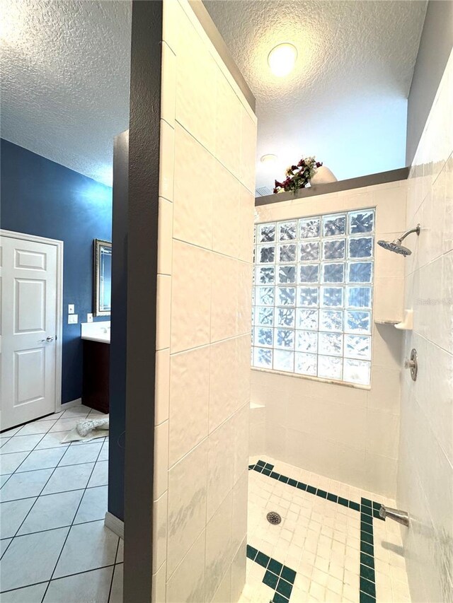 full bathroom with tile patterned flooring, tiled shower, vanity, and a textured ceiling