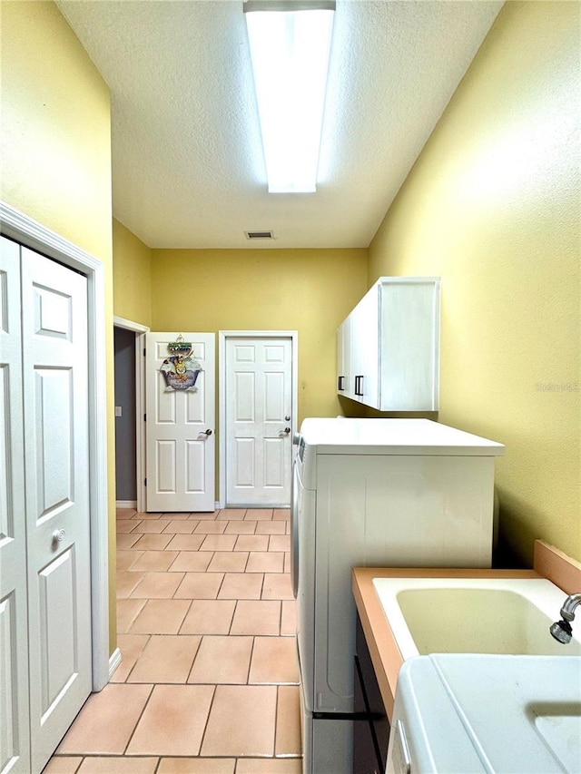 washroom with a textured ceiling, light tile patterned flooring, washing machine and dryer, and cabinet space