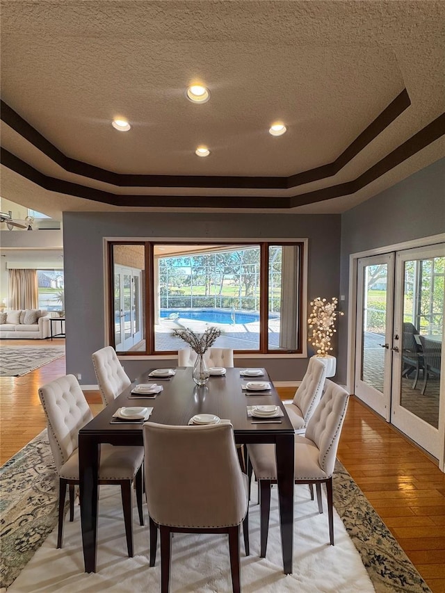 dining area with a tray ceiling, french doors, a textured ceiling, and light wood finished floors