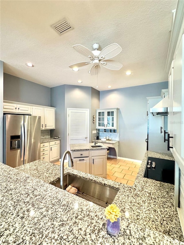 kitchen featuring visible vents, light stone countertops, black electric stovetop, stainless steel refrigerator with ice dispenser, and a sink