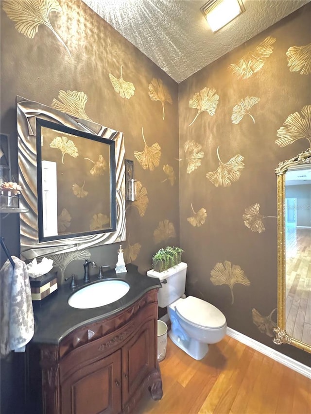 half bath with toilet, a textured ceiling, vanity, wood finished floors, and baseboards