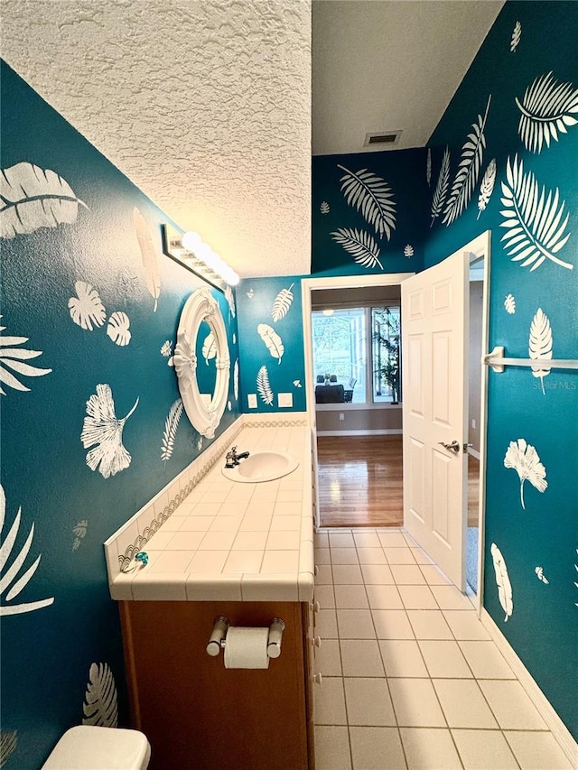 bathroom featuring visible vents, vanity, a textured ceiling, baseboards, and tile patterned floors