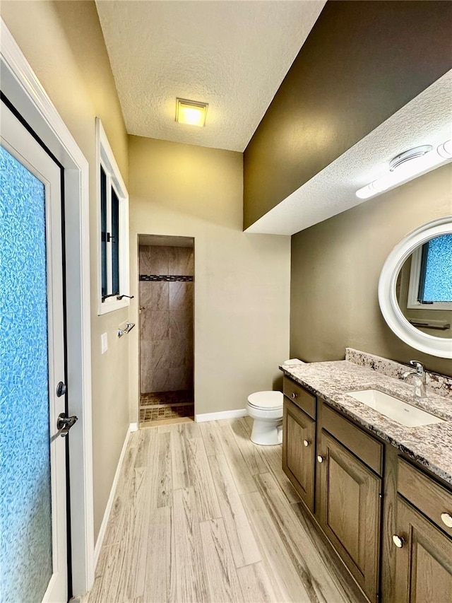 full bath featuring toilet, vanity, a textured ceiling, wood finished floors, and tiled shower