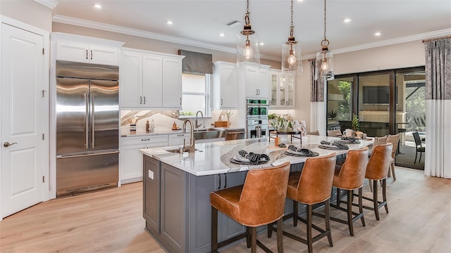 kitchen with appliances with stainless steel finishes, a wealth of natural light, white cabinets, and an island with sink