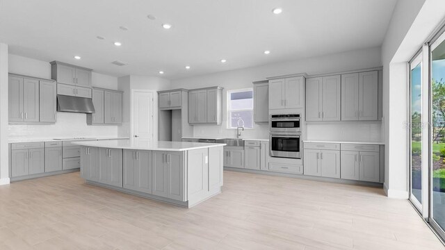 5646 Nevis Ter, Kissimmee, FL 34758 - kitchen with gray cabinets, under cabinet range hood, stainless steel double oven, recessed lighting, and stovetop