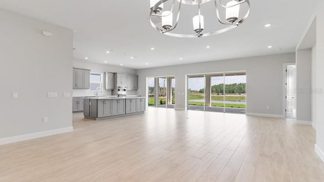 5646 Nevis Ter, Kissimmee, FL 34758 - unfurnished living room with a sink, baseboards, light wood-style floors, a chandelier, and recessed lighting