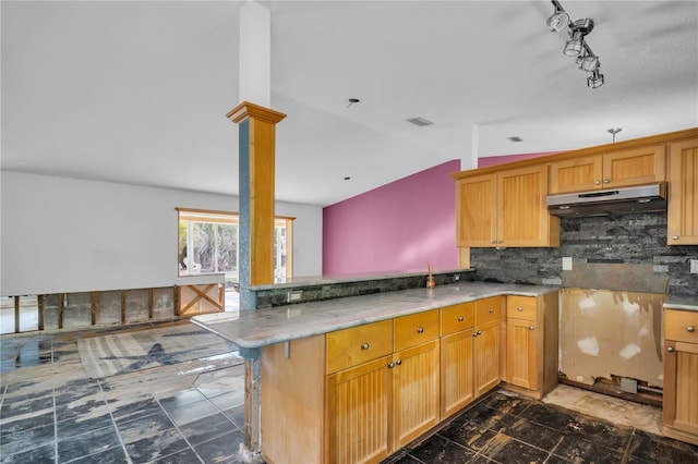 kitchen featuring under cabinet range hood, a peninsula, vaulted ceiling, backsplash, and ornate columns