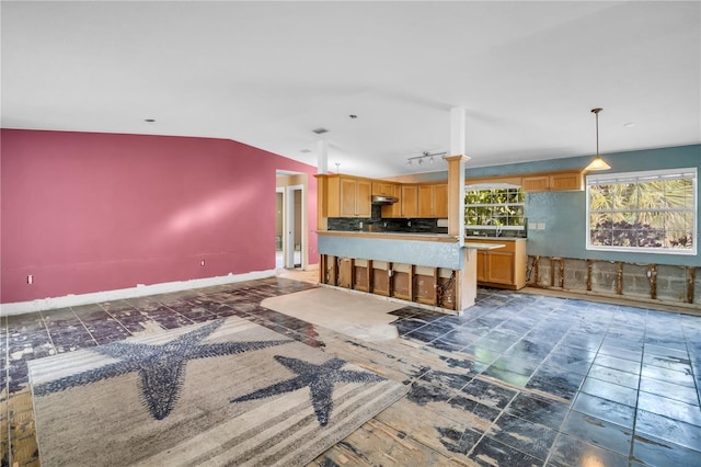 kitchen featuring baseboards, lofted ceiling, under cabinet range hood, pendant lighting, and a sink