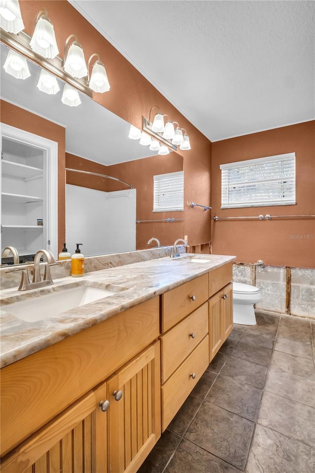 full bath with double vanity, a sink, toilet, and tile patterned floors