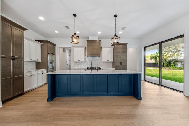 kitchen featuring custom exhaust hood, light countertops, visible vents, light wood-type flooring, and stainless steel fridge with ice dispenser