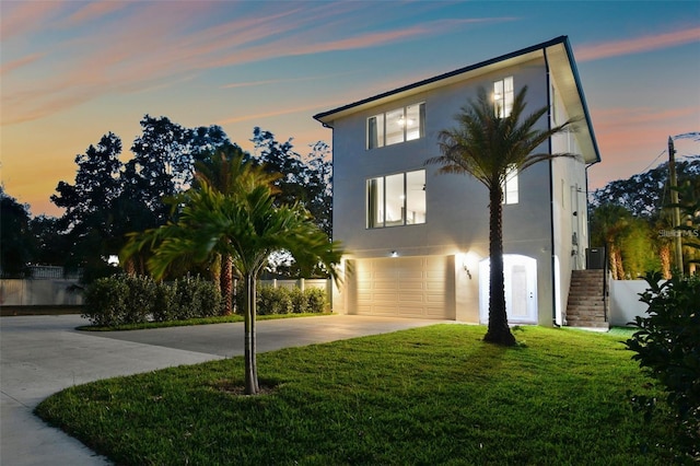 contemporary house featuring a garage, a lawn, concrete driveway, stairs, and stucco siding