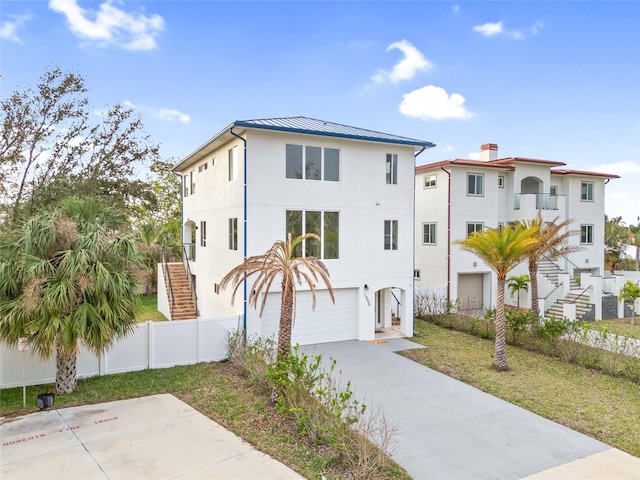 coastal inspired home with fence, a garage, stucco siding, a standing seam roof, and stairs