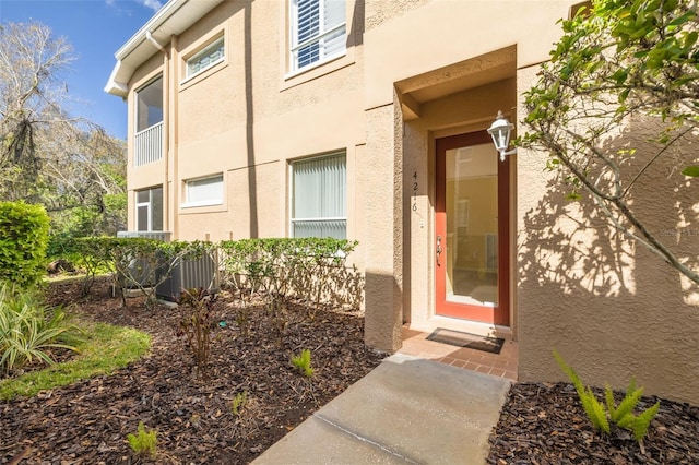 view of exterior entry with cooling unit and stucco siding