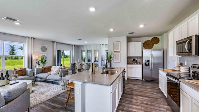 kitchen with dark wood finished floors, appliances with stainless steel finishes, open floor plan, a kitchen bar, and a sink