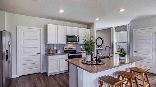 kitchen with a breakfast bar, backsplash, appliances with stainless steel finishes, dark wood-type flooring, and white cabinetry