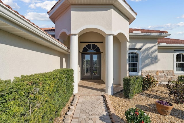 property entrance featuring stone siding, french doors, a tile roof, and stucco siding