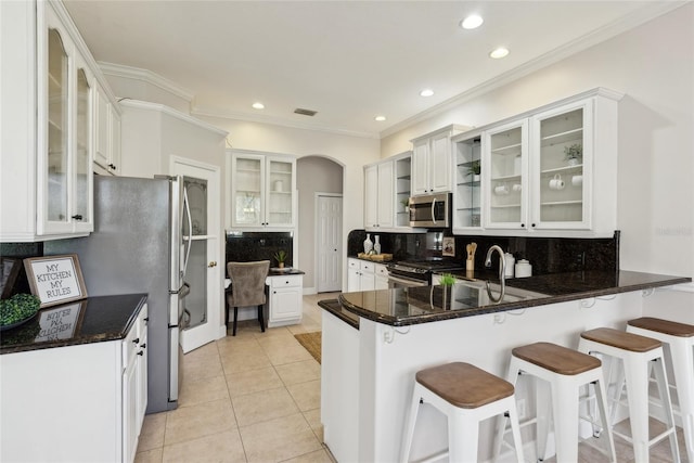 kitchen with arched walkways, light tile patterned floors, stainless steel appliances, a peninsula, and a breakfast bar