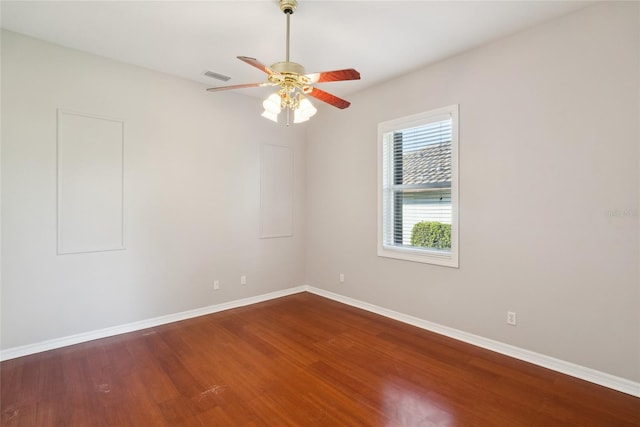 empty room with a ceiling fan, wood finished floors, visible vents, and baseboards