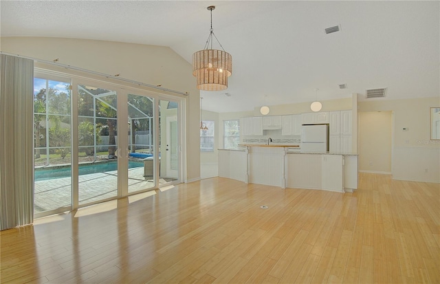 interior space featuring an inviting chandelier, lofted ceiling, light wood-style flooring, and visible vents
