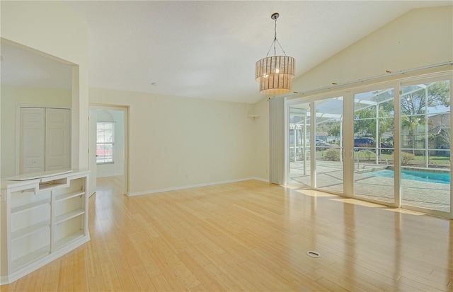 unfurnished room with light wood-type flooring, baseboards, a chandelier, and vaulted ceiling