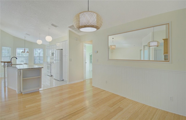 unfurnished living room featuring a sink, a textured ceiling, light wood-style floors, wainscoting, and vaulted ceiling