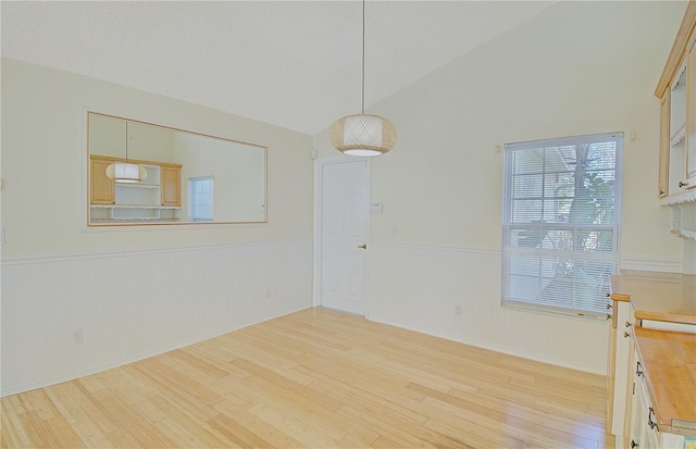 spare room with light wood-type flooring, a wainscoted wall, and lofted ceiling