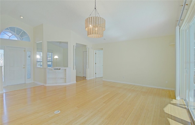 interior space with a chandelier, light wood-style flooring, lofted ceiling, and baseboards