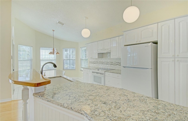 kitchen with white appliances, light stone countertops, a sink, vaulted ceiling, and white cabinets