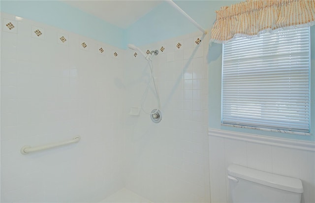 bathroom featuring toilet, tiled shower, and wainscoting