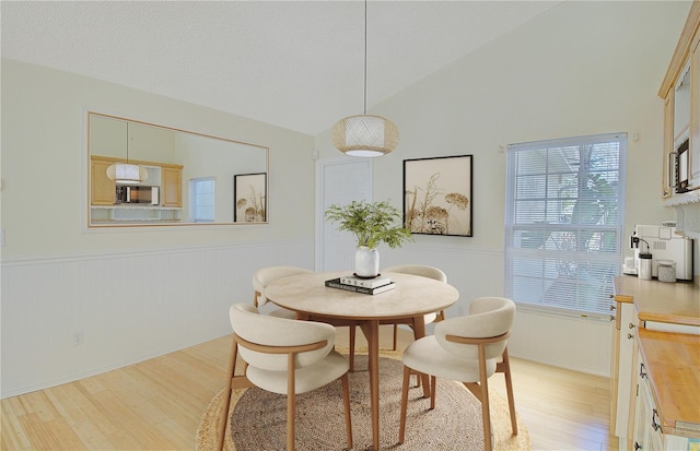 dining area with a wainscoted wall, a textured ceiling, light wood-style floors, and lofted ceiling