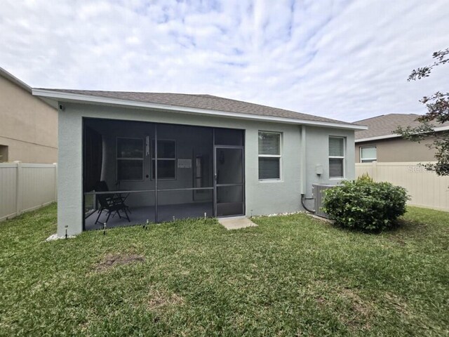 back of house with stucco siding, central AC, fence, a yard, and a sunroom