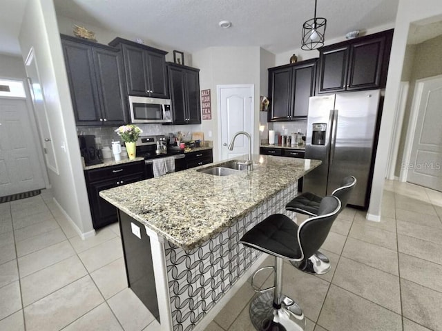 kitchen featuring a breakfast bar area, light stone counters, light tile patterned floors, a sink, and appliances with stainless steel finishes