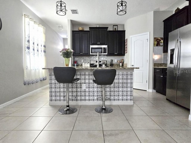 kitchen featuring light tile patterned floors, stainless steel appliances, tasteful backsplash, and a breakfast bar