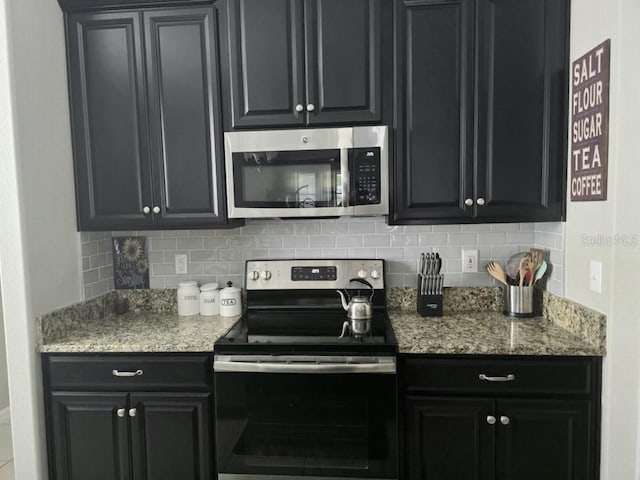 kitchen featuring decorative backsplash, light stone countertops, appliances with stainless steel finishes, and dark cabinets