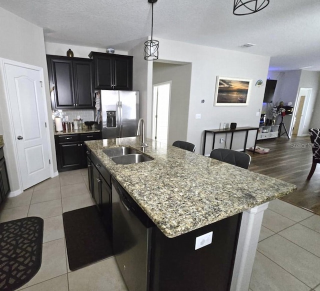 kitchen with light tile patterned floors, stainless steel appliances, light stone counters, and a sink