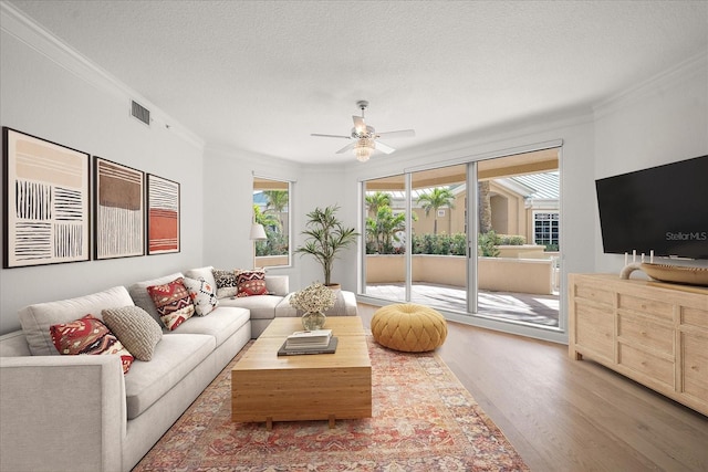 living area with visible vents, ceiling fan, ornamental molding, wood finished floors, and a textured ceiling