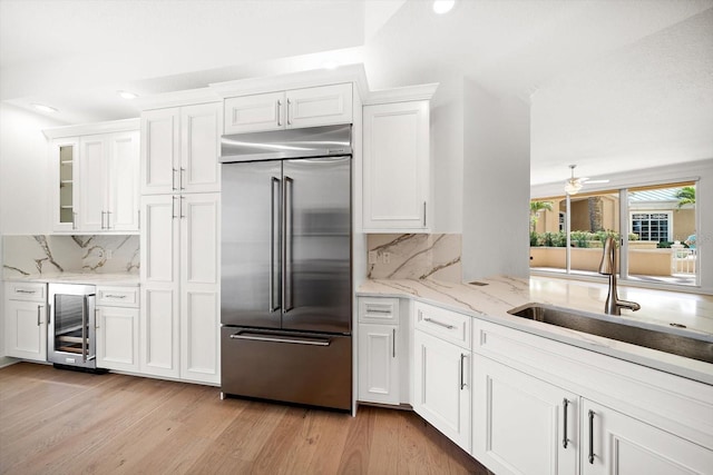 kitchen featuring white cabinets, beverage cooler, a sink, light wood-type flooring, and stainless steel built in refrigerator