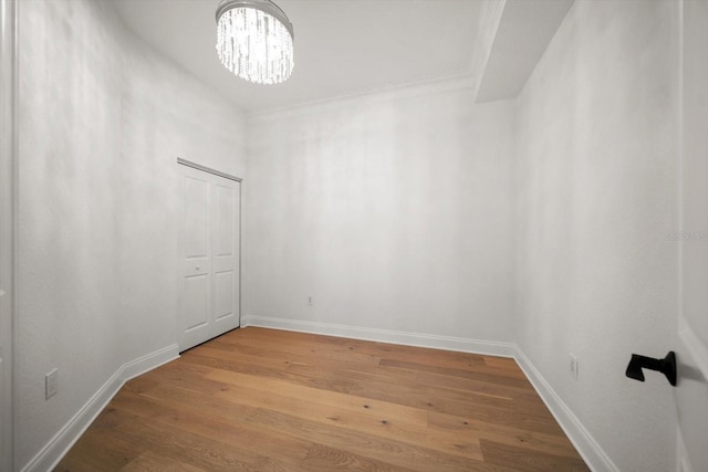 spare room with a chandelier, ornamental molding, wood finished floors, and baseboards